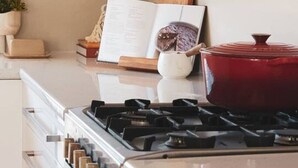A kitchen with a stove, oven, and a red pot on the counter.
