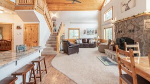 A spacious living area with a stone fireplace, wooden ceiling, and a staircase leading to an upper level. - Red Feather Woodland Retreat, Family and Pet Friendly, 4 beds (Red Feather Lakes)