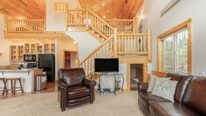 A spacious living area with a wooden staircase, a leather sofa, a television, and a kitchen area. - Red Feather Woodland Retreat, Family and Pet Friendly, 4 beds (Red Feather Lakes)