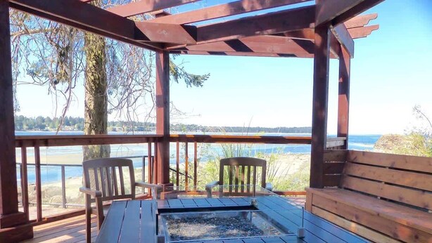 Um deck de madeira com hidromassagem, duas cadeiras e vista para um lago.