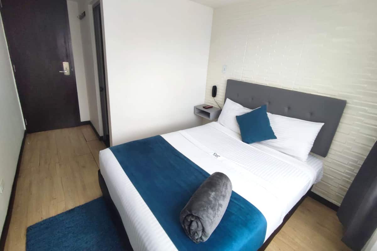 Une chambre d’hôtel avec un lit, une table de chevet, un téléphone et une porte.
