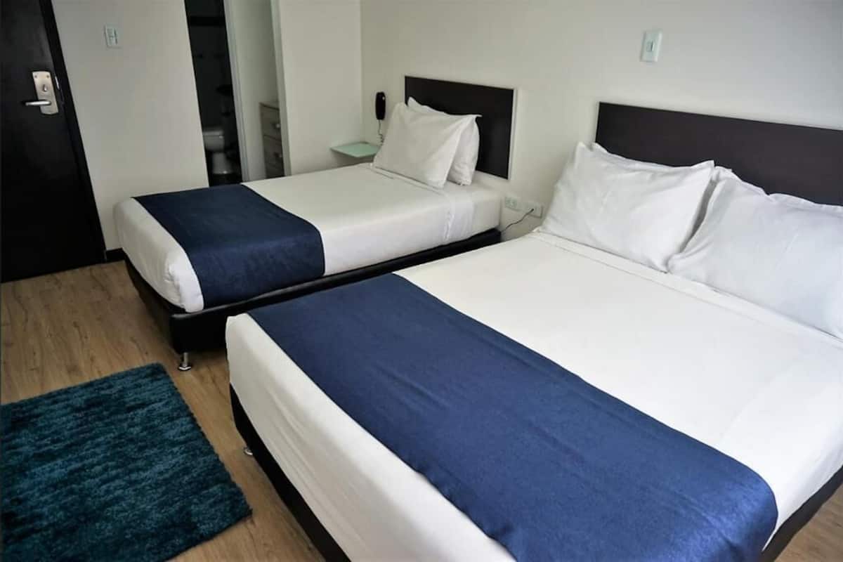 Deux lits simples avec du linge de lit blanc et des couvre-lits bleu foncé dans une chambre d’hôtel.