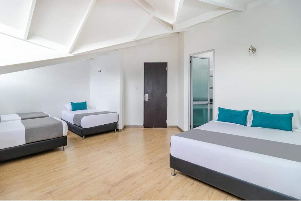 Une chambre d’hôtel moderne avec un plafond en pente, un grand lit, deux petits lits et une porte donnant accès à la salle de bain.