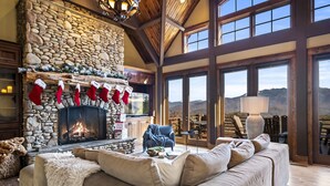 A cozy living room with a stone fireplace, a large window overlooking mountains, and a plush sofa. - Renowned Architect! VIEWS/Theatre/Game/HotTub/FirePit/Harry Potter (Gatlinburg)