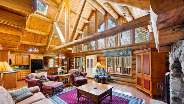 A spacious log cabin interior with a high ceiling, wooden walls, a large dining area, and a cozy living room with leather furniture. - Charming 3-bedroom Log Cabin by the lake (Egg Harbor)