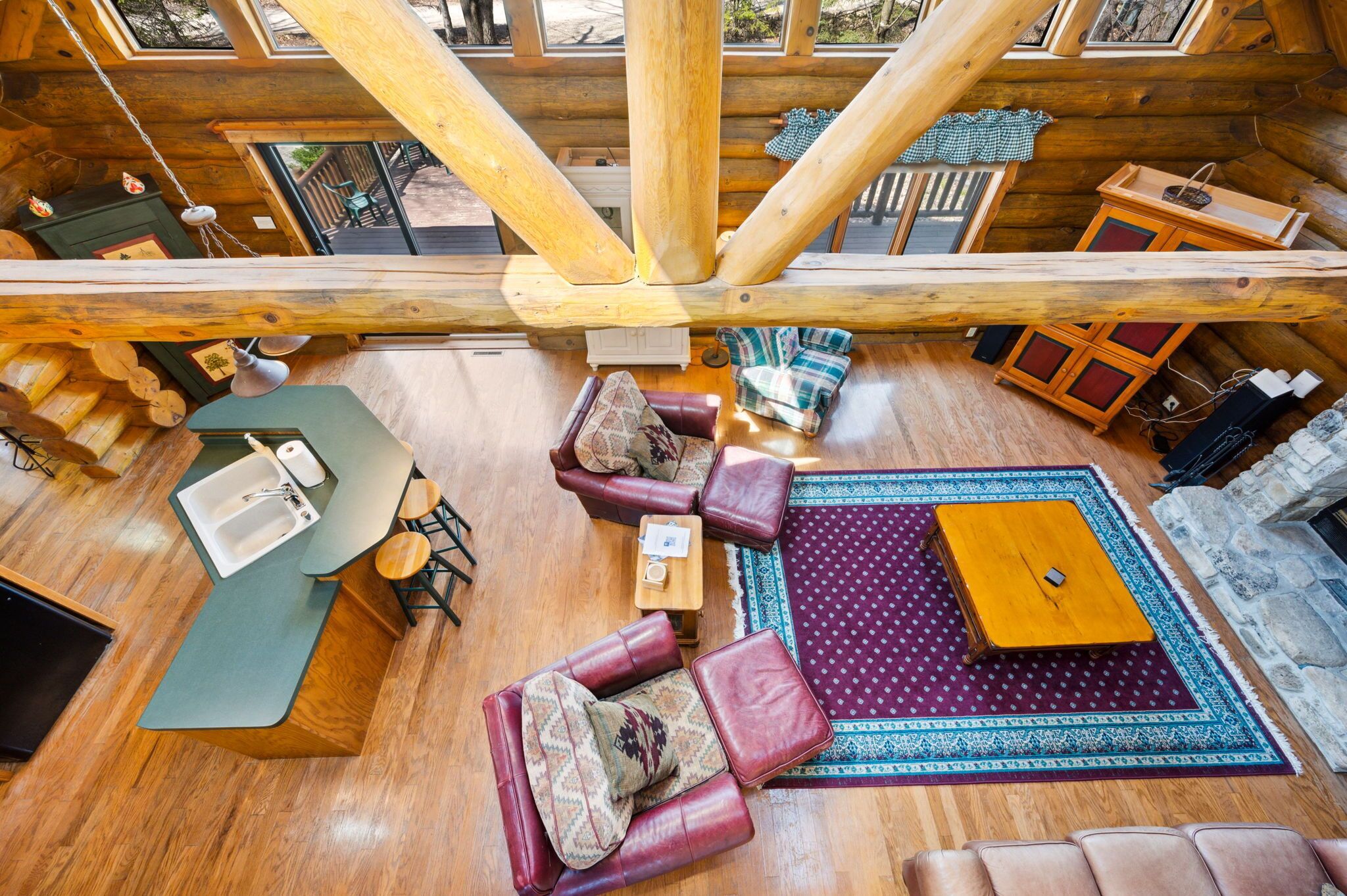 A log cabin interior with a wooden dining table, leather sofas, a wooden coffee table, and a stone fireplace.