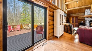 A log cabin interior with a large sliding glass door leading to an outdoor deck with chairs and a fire pit. - Charming 3-bedroom Log Cabin by the lake (Egg Harbor)