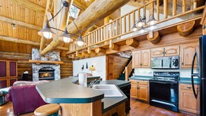A log cabin interior with a stone fireplace, wooden dining area, and a kitchen with modern appliances. - Charming 3-bedroom Log Cabin by the lake (Egg Harbor)
