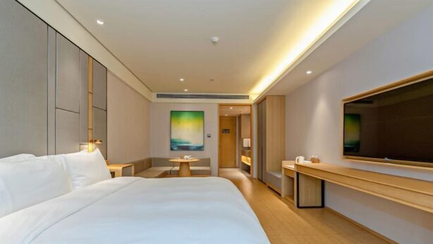 Una habitación de hotel moderna con una cama grande, un escritorio, una silla y un televisor en la pared.