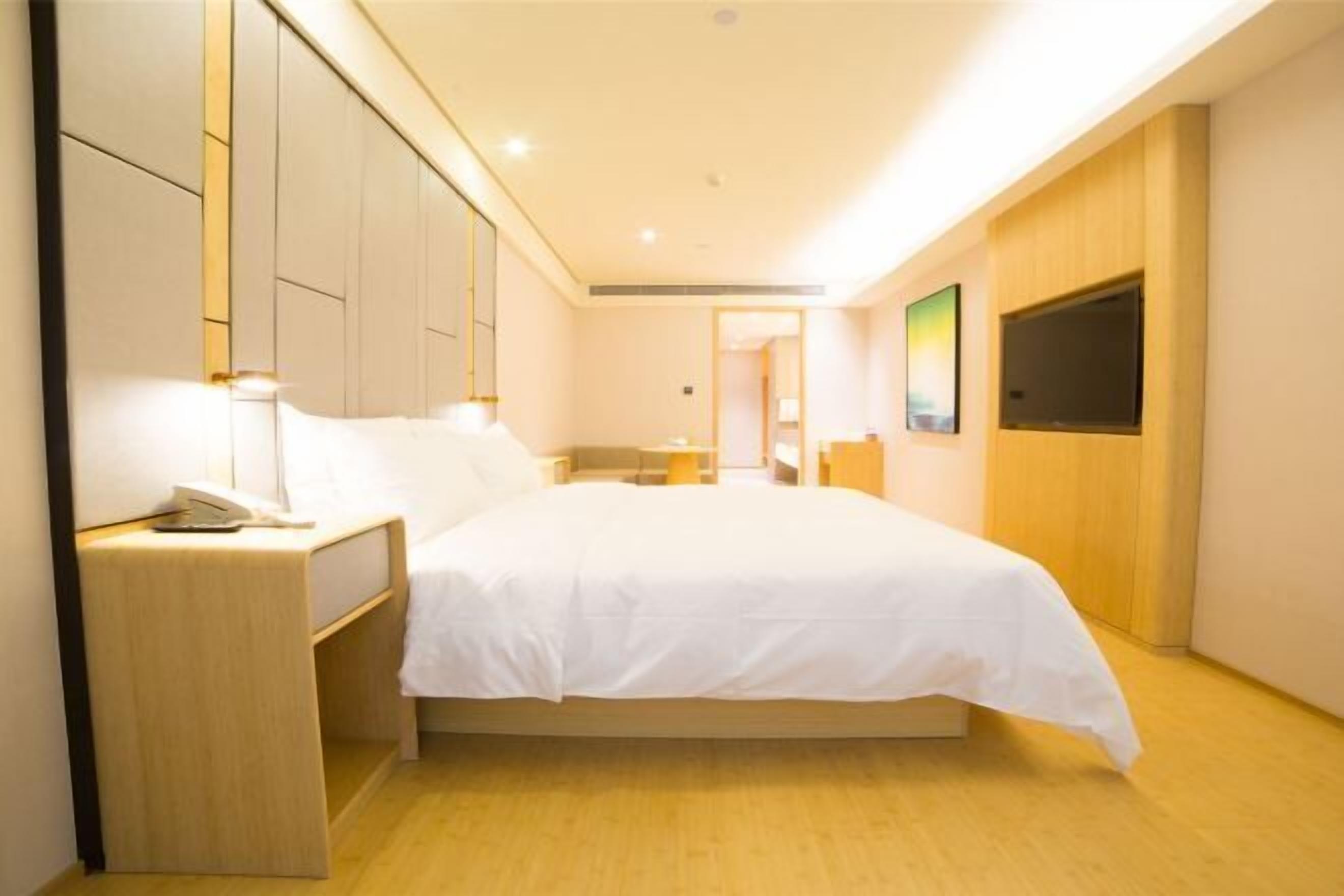 A hotel room with a bed, bedside table, and a TV mounted on the wall.