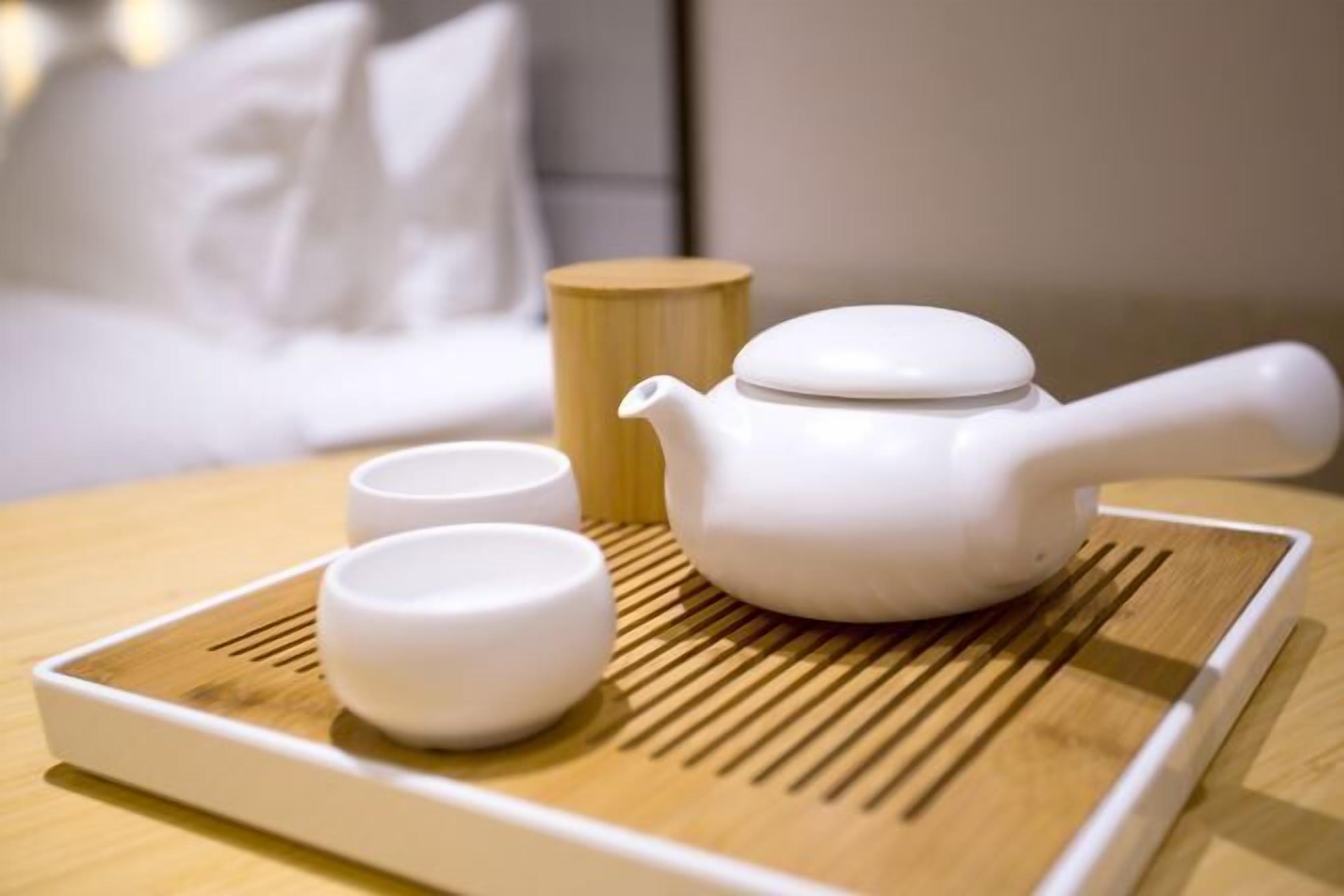 A white teapot and two white cups on a tray with a bamboo mat.