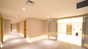 Pasillo de hotel con suelo estampado, iluminación empotrada y puerta de ascensor de vidrio.