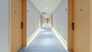 Un pasillo largo y estrecho con puertas de madera a ambos lados, piso de baldosas e iluminación empotrada en el techo.