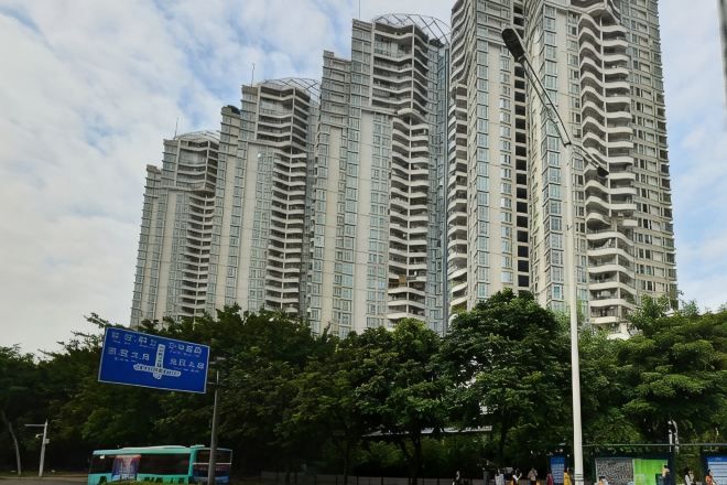 Een hoog appartementencomplex met meerdere balkons, een straatnaambord en bomen op de voorgrond.