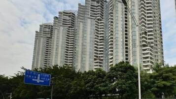 Een hoog appartementencomplex met meerdere balkons, een straatnaambord en bomen op de voorgrond.