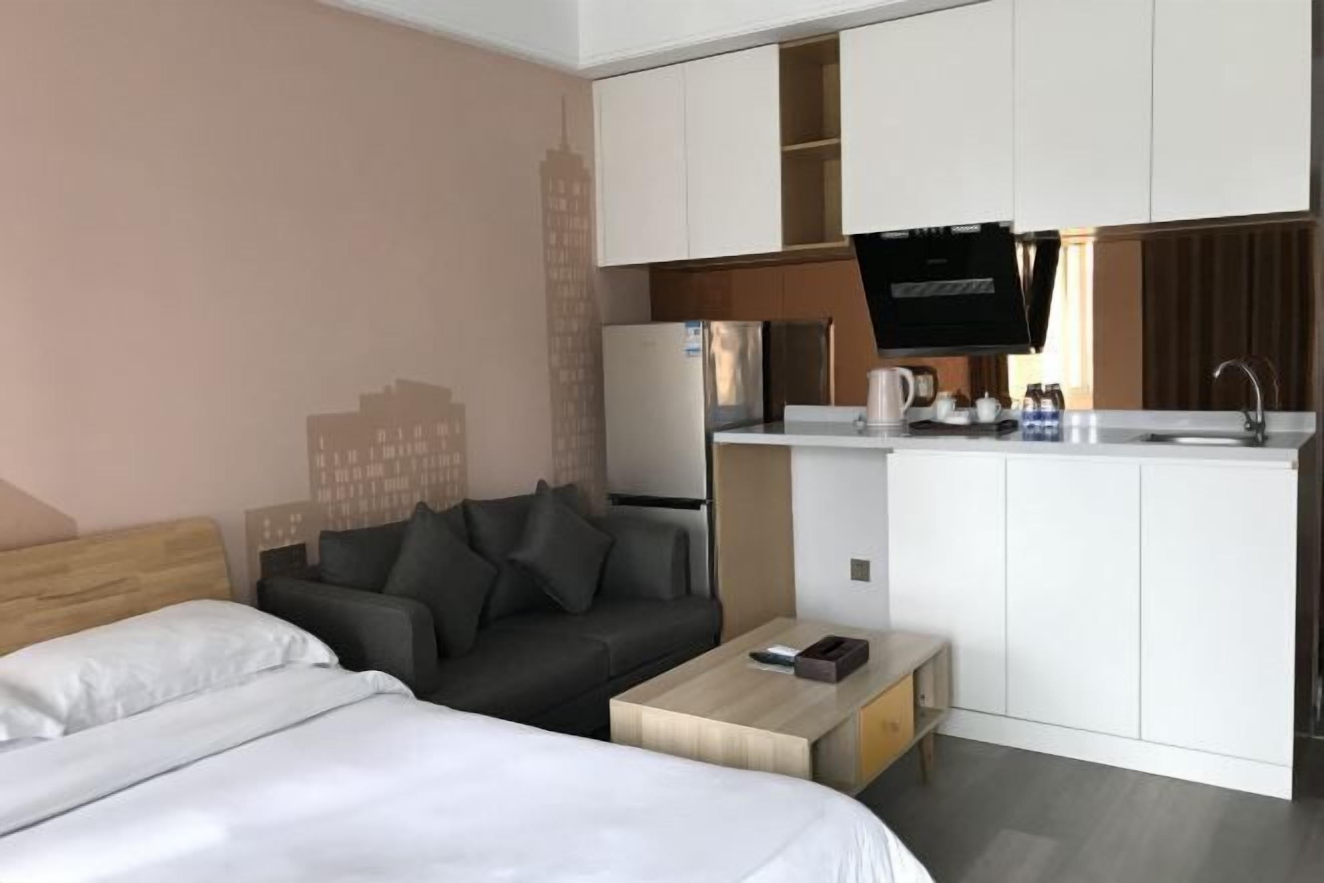 A hotel room with a bed, a sofa, a small coffee table, a kitchenette with a refrigerator, a microwave, and a sink.
