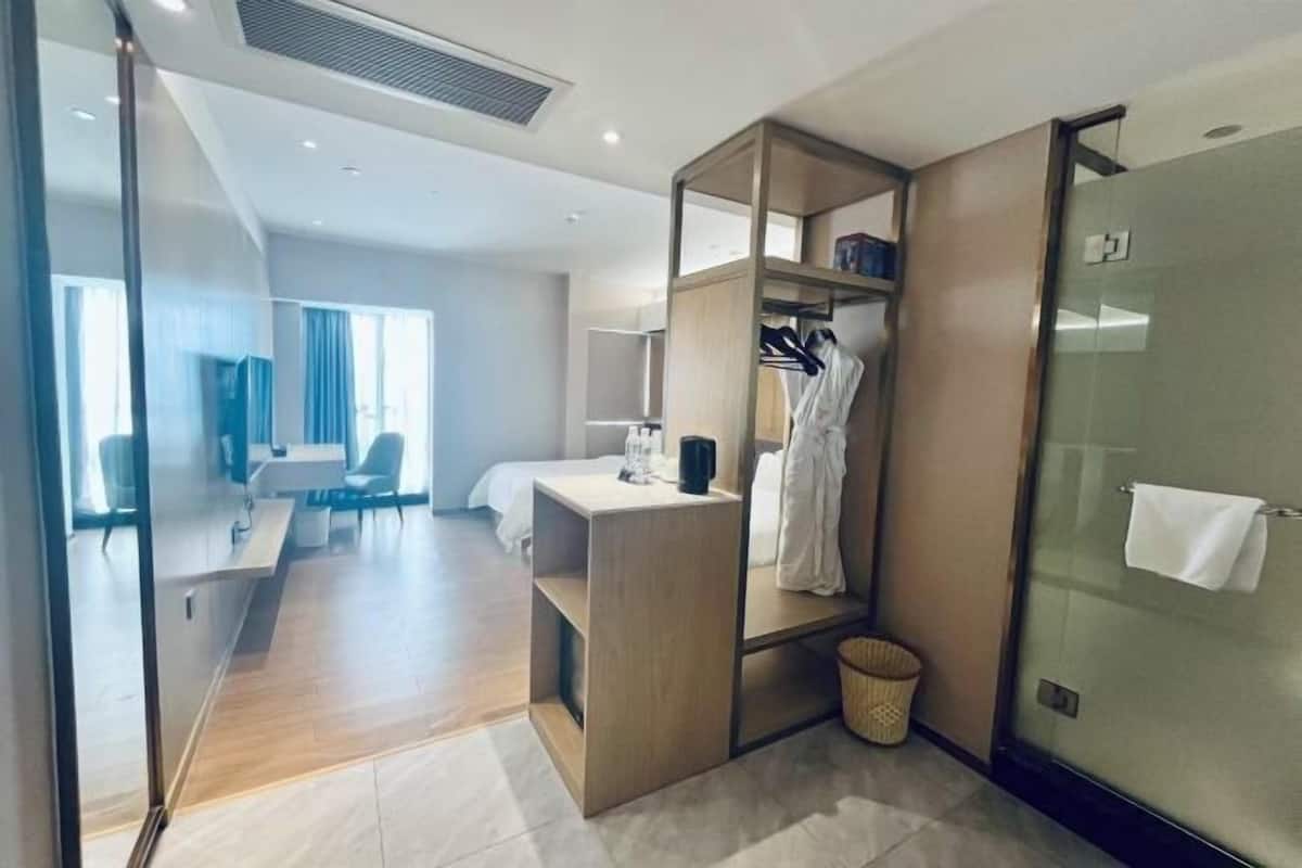 A modern hotel room with a wooden desk, a bed, a seating area with chairs, and a glass shower enclosure.