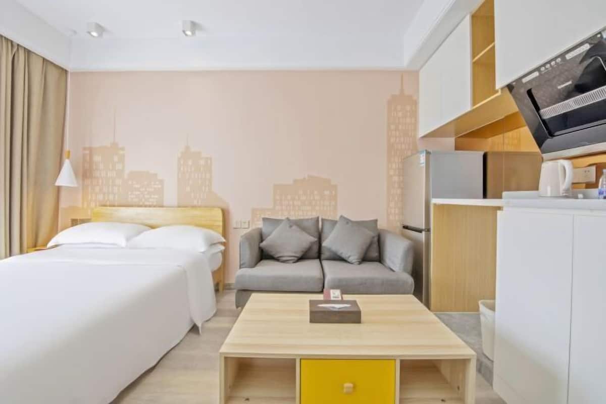 A hotel room with a bed, a sofa, a coffee table, a TV, and a kitchenette.