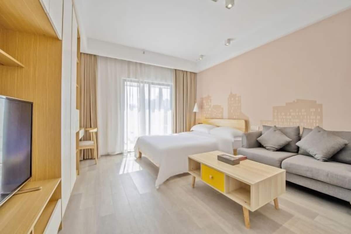 A modern hotel room with a bed, a sofa, a TV, and a wooden coffee table.