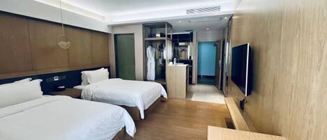 Ein Hotelzimmer mit zwei Betten, einem Fernseher, einem Holztisch und einem begehbaren Kleiderschrank.