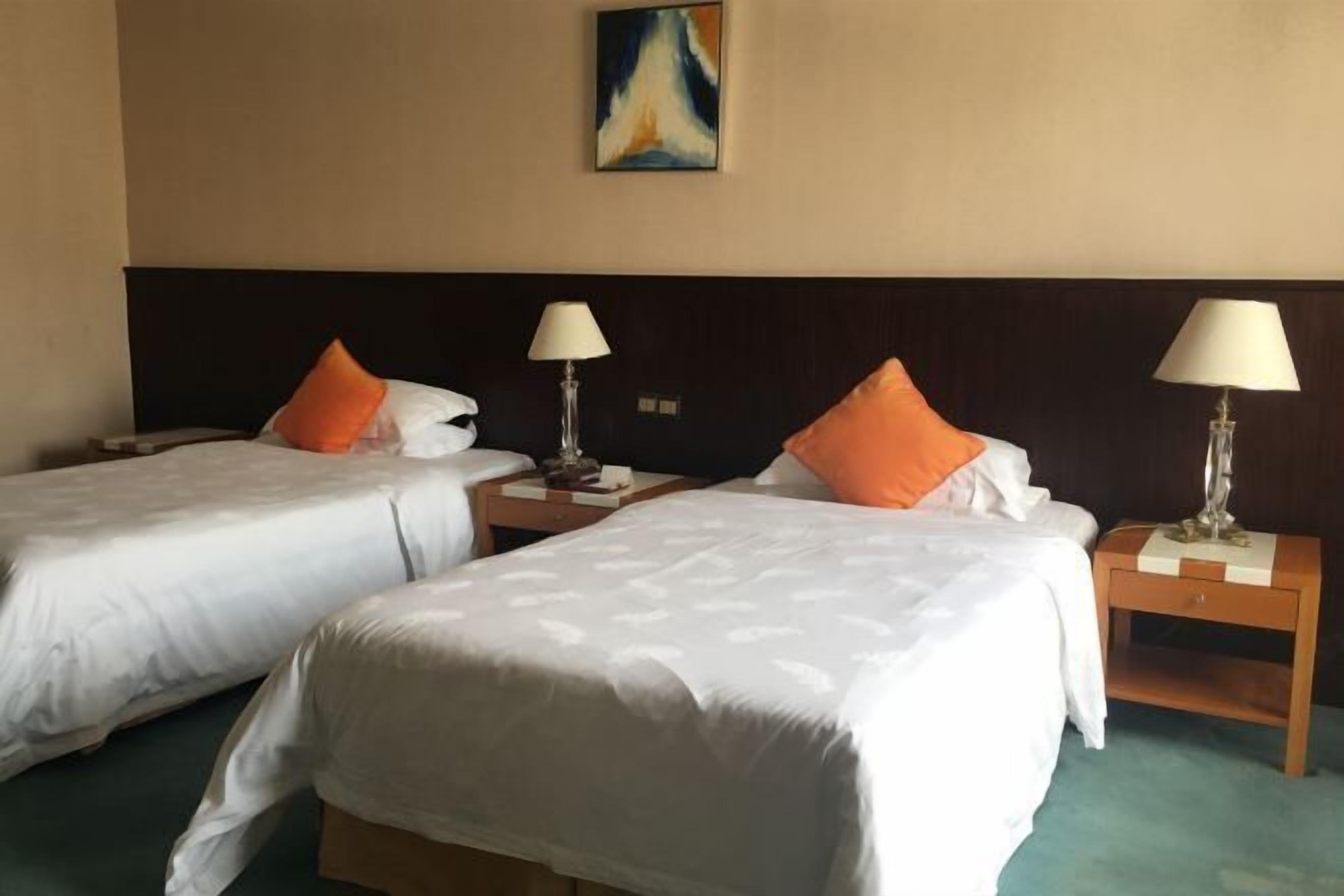 A hotel room with two beds, each with white bedding and orange pillows, and bedside lamps.