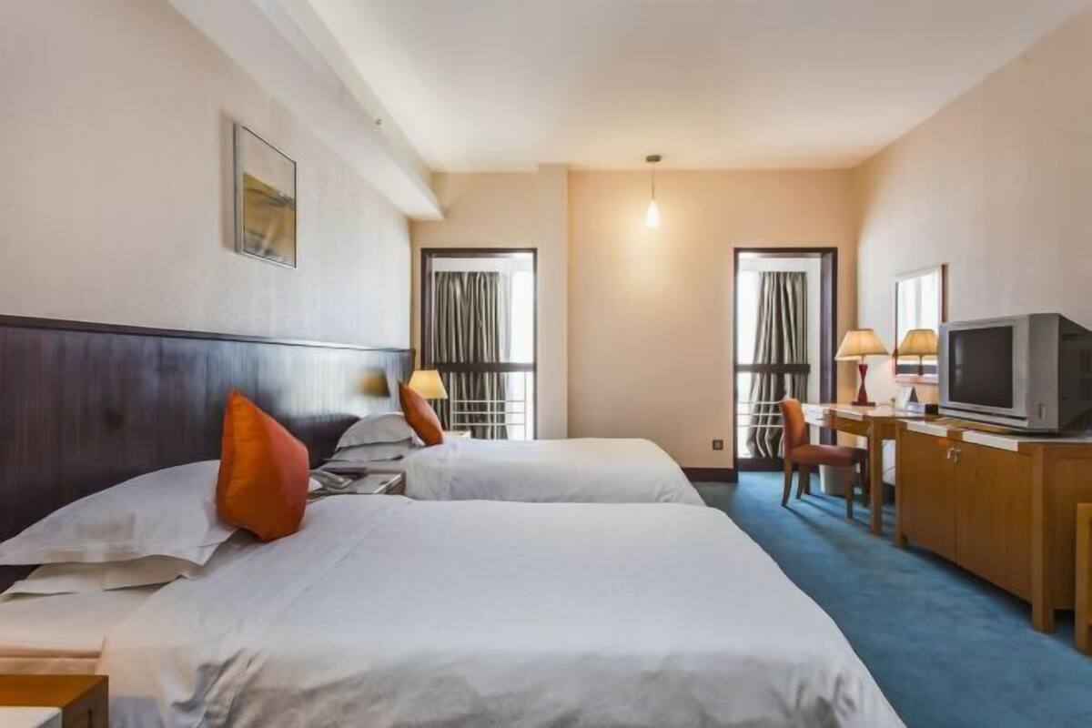 A hotel room with two beds, a desk, a television, and a window with curtains.