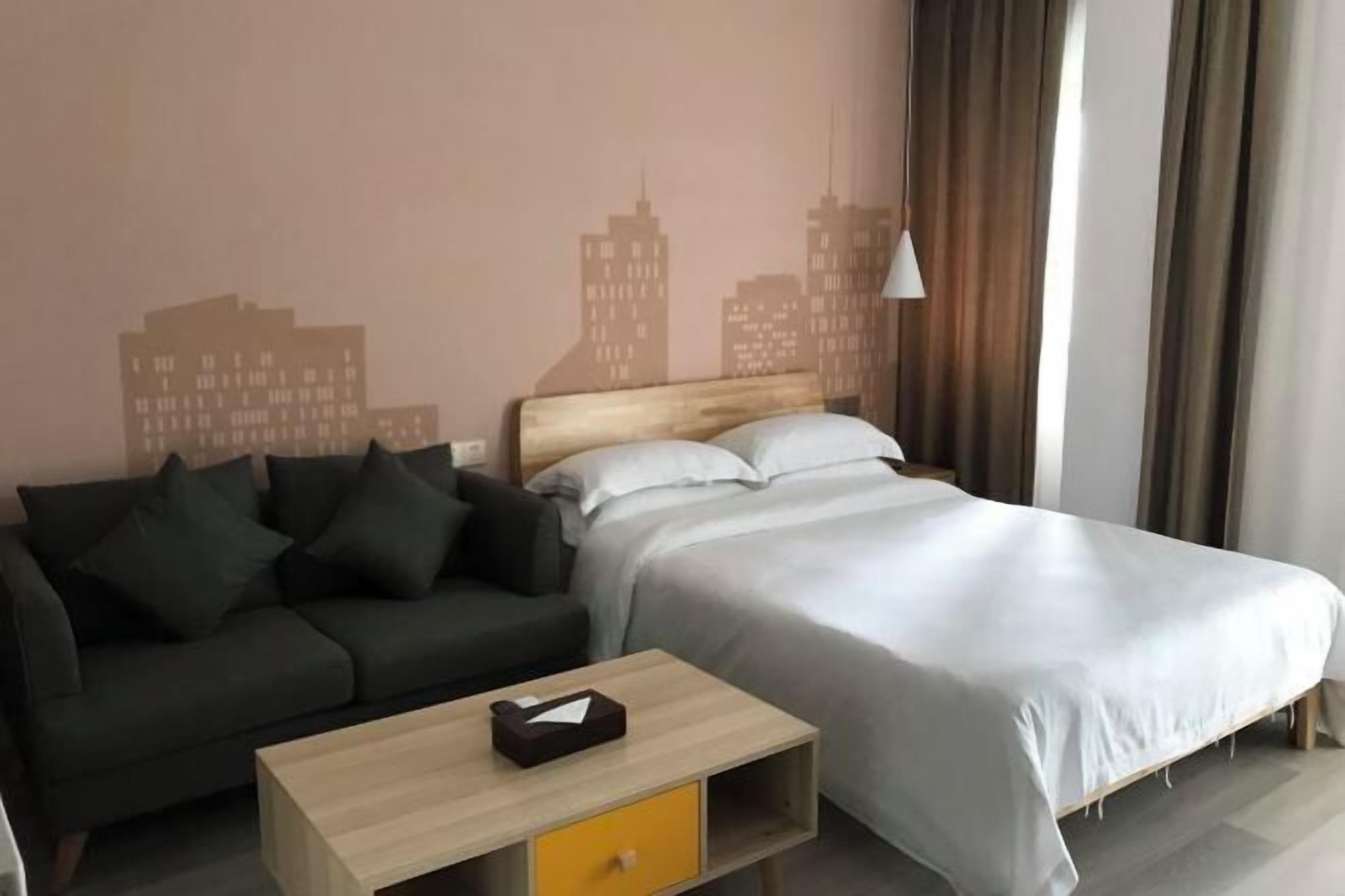 A hotel room with a bed, a sofa, a small table, and a cityscape wall mural.