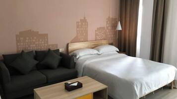 A hotel room with a bed, a sofa, a small table, and a cityscape wall mural.
