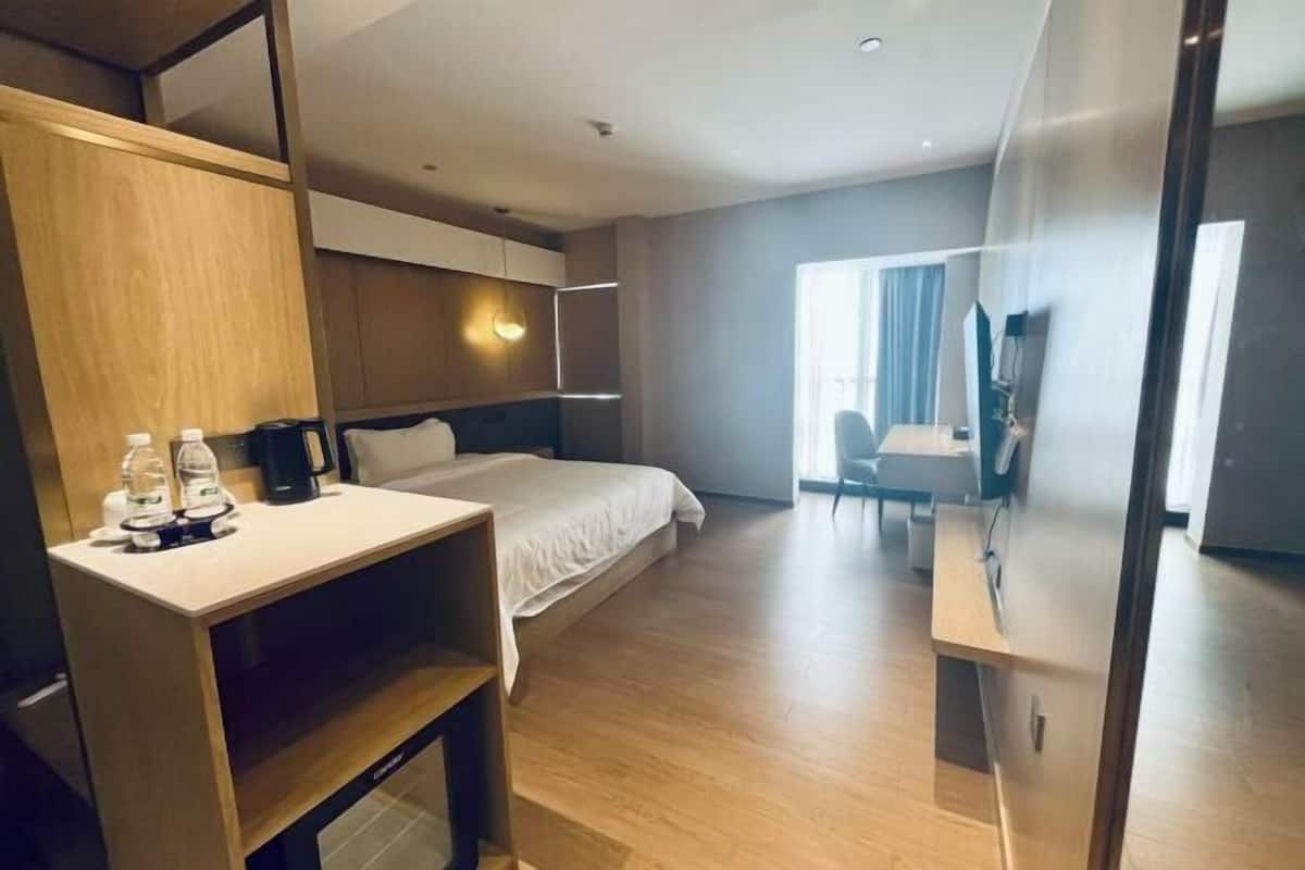 A modern hotel room with a bed, a desk, a chair, a TV, and a large mirror.
