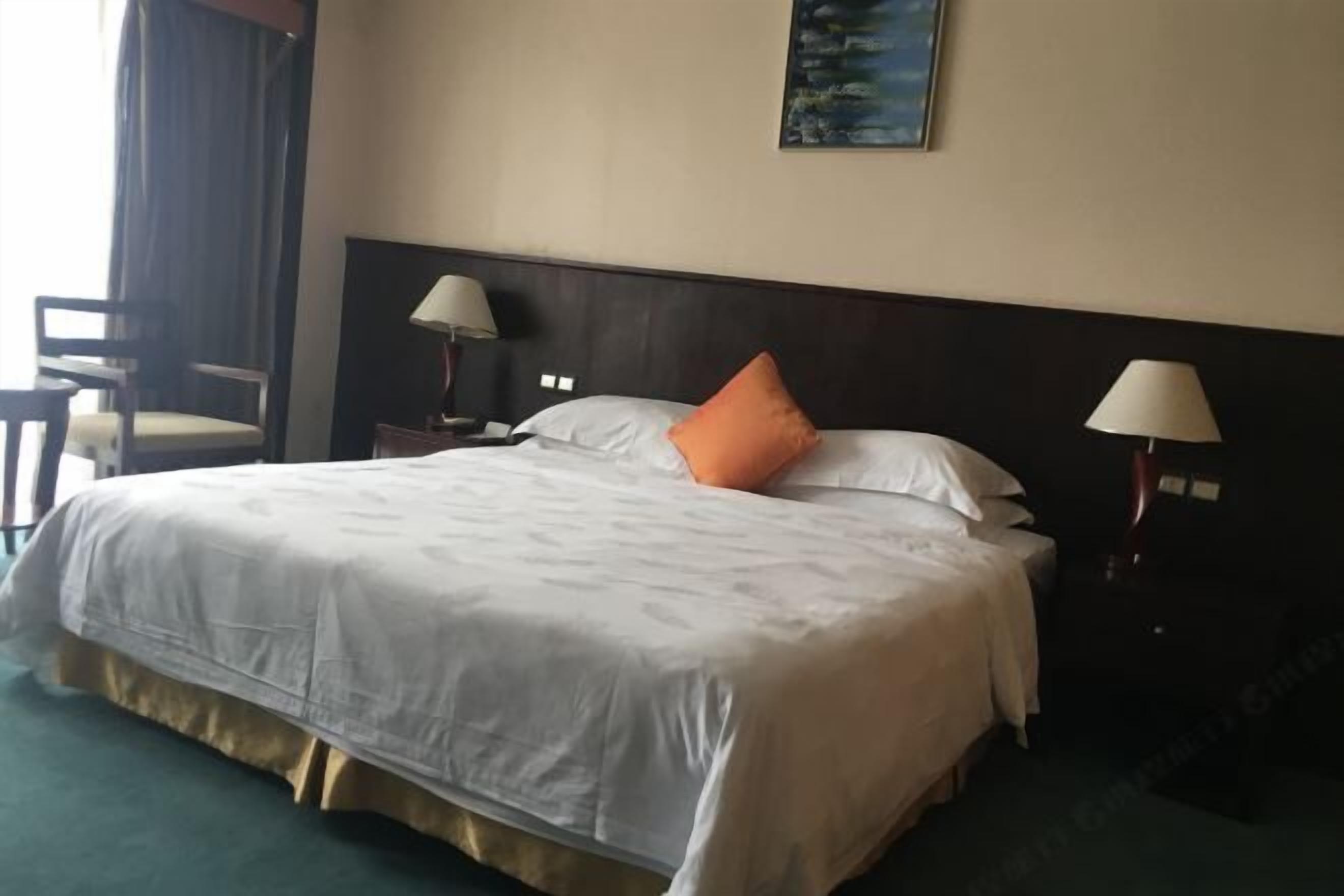 Quarto de hotel com uma cama grande, duas luminárias de cabeceira, uma cadeira e um quadro na parede.