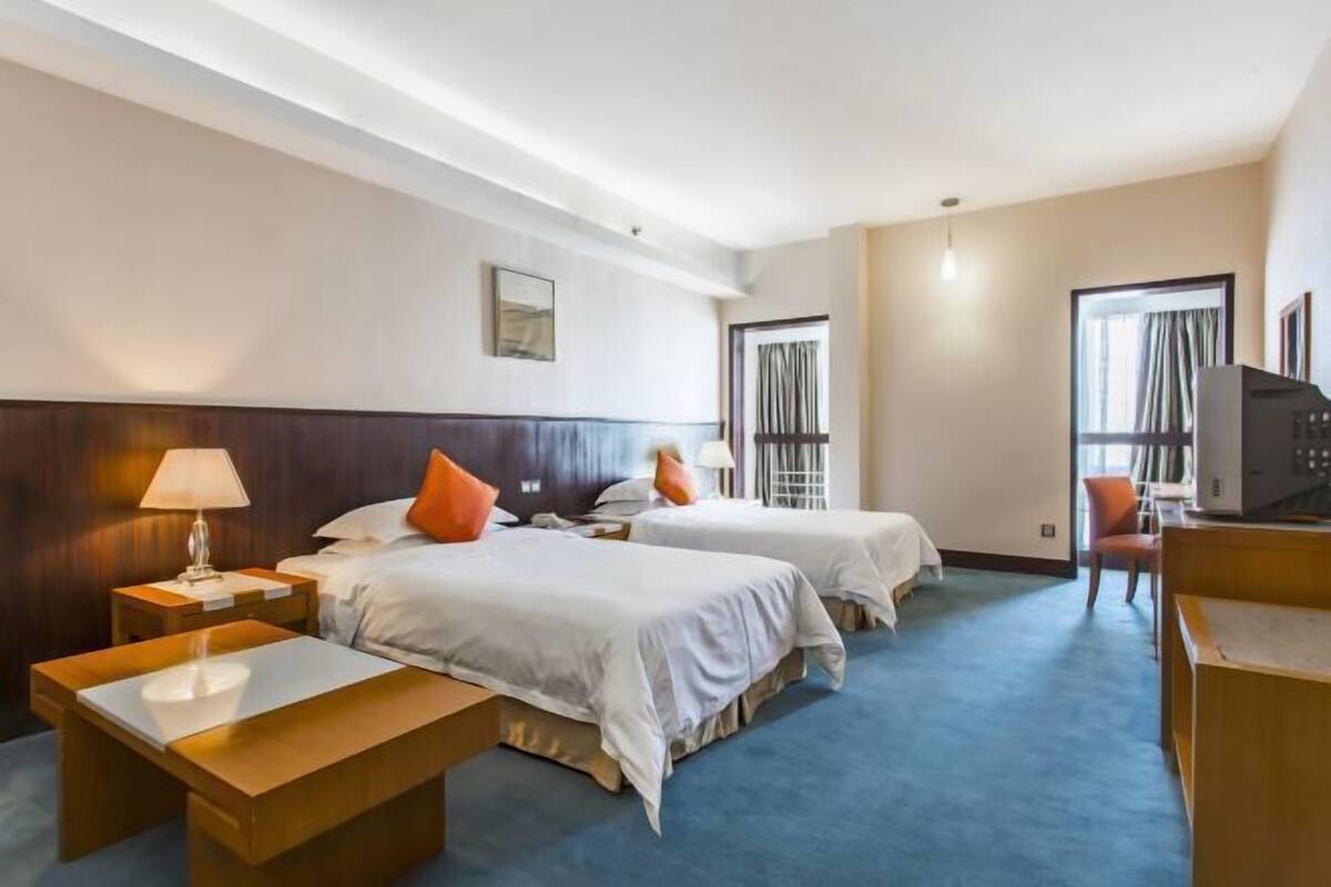 A hotel room with two beds, a desk, a chair, and a TV.