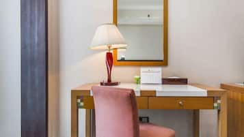 Habitación de hotel con un escritorio de madera, una lámpara, un espejo y una silla rosa.