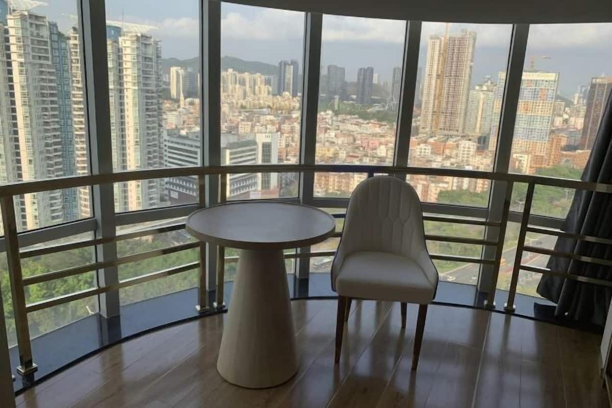 A room with a large window offering a city view, a round table, and a single chair.