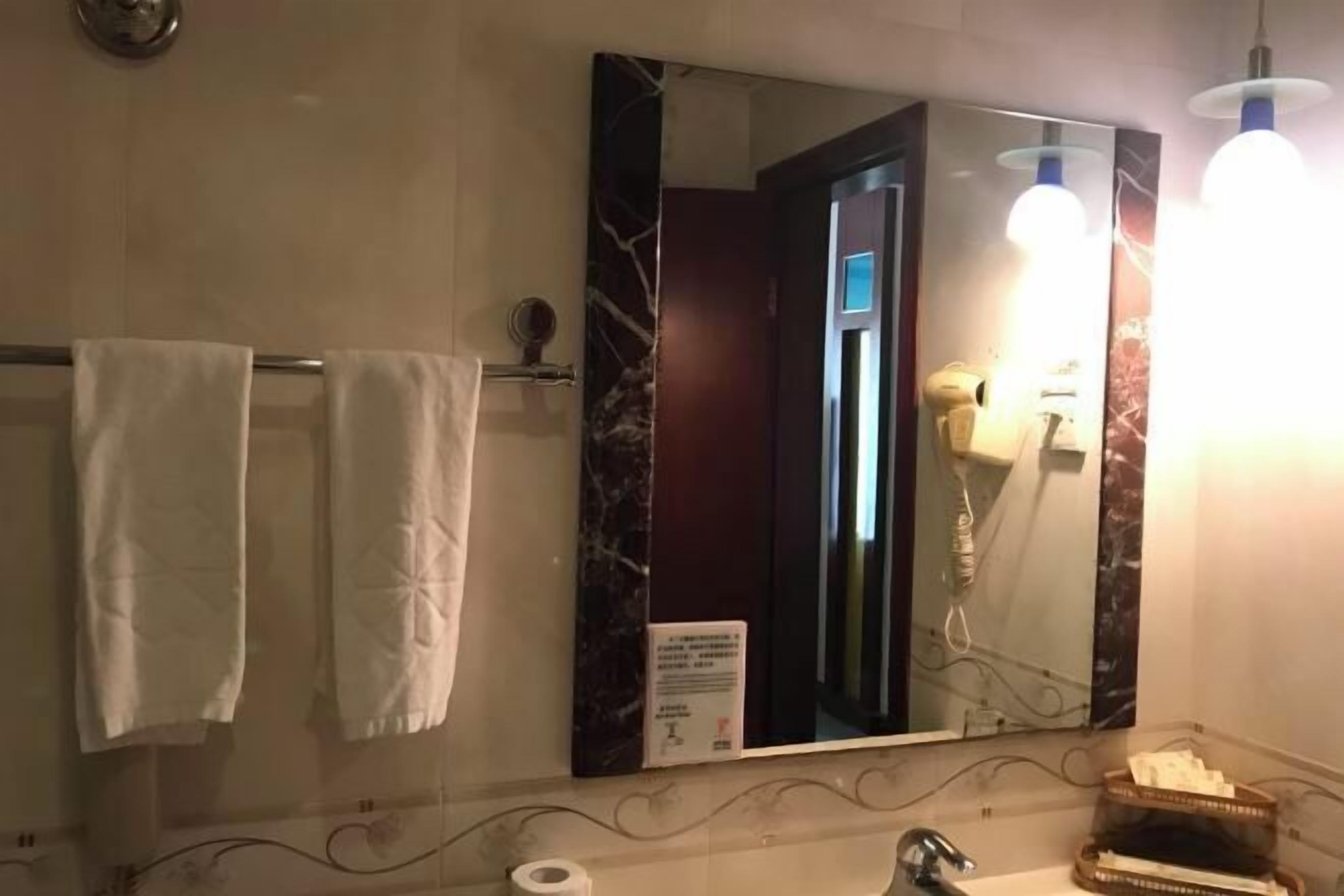 A bathroom with a large mirror, two towels, a sink, and a light fixture.