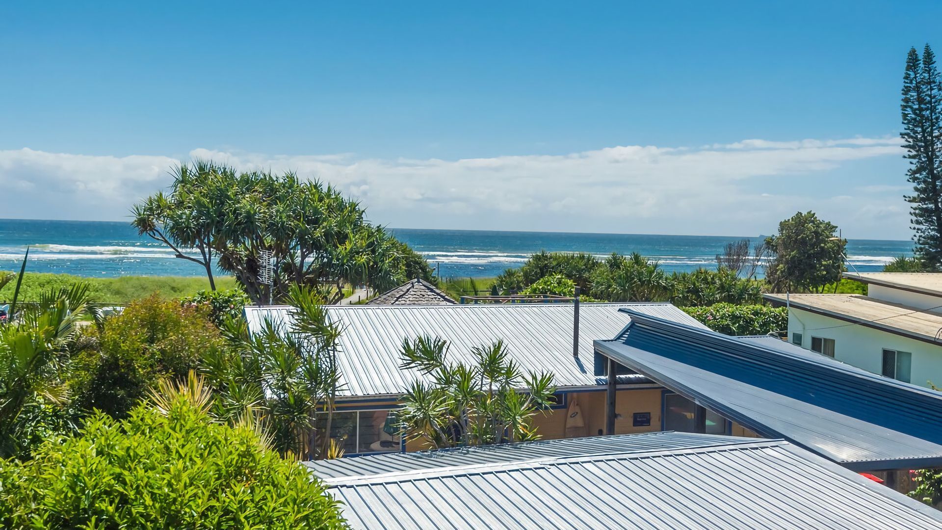 A coastal view with a house overlooking the ocean, surrounded by greenery and a clear sky.