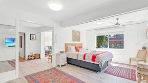 A modern bedroom with a large bed, a ceiling fan, and a view of greenery through the window. - Beach Views - Spacious home by the ocean (Lennox Head)