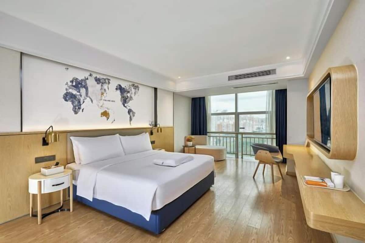 Ein Hotelzimmer mit einem großen Bett, einem Schreibtisch, einem Sessel, einem Fernseher und einer Weltkarte an der Wand.