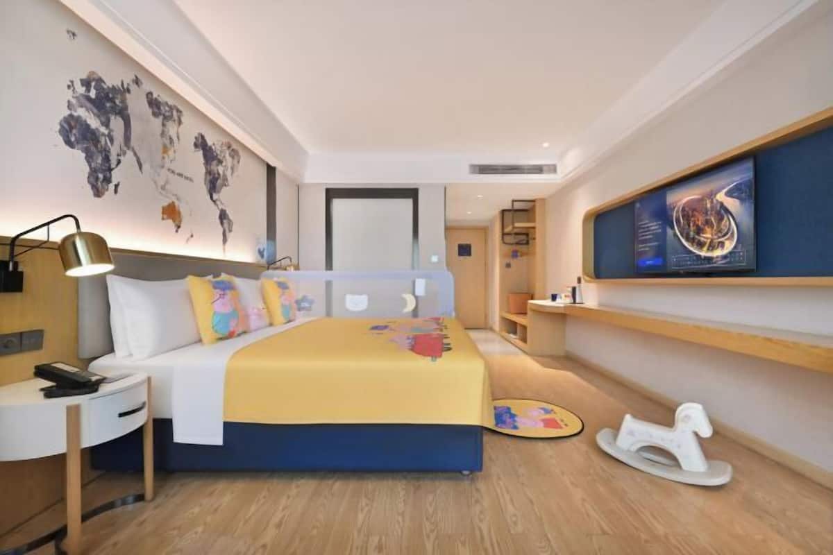 Ein modernes Hotelzimmer mit Bett, Nachttisch, Lampe, Kunstwerk und Fernseher.
