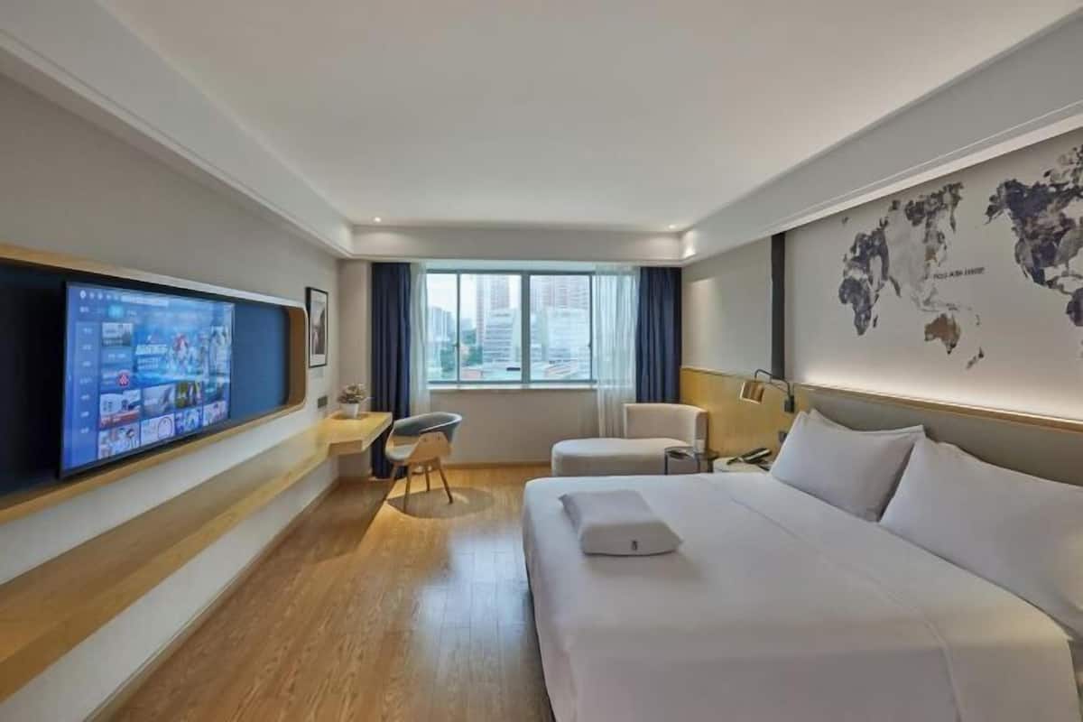Ein Hotelzimmer mit Bett, Schreibtisch, Stuhl, Fernseher und einem fensterbepflanzten Fenster.