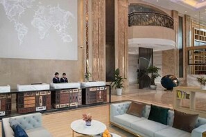 A hotel lobby with seating areas, a reception desk, and a large world map projection on the wall.