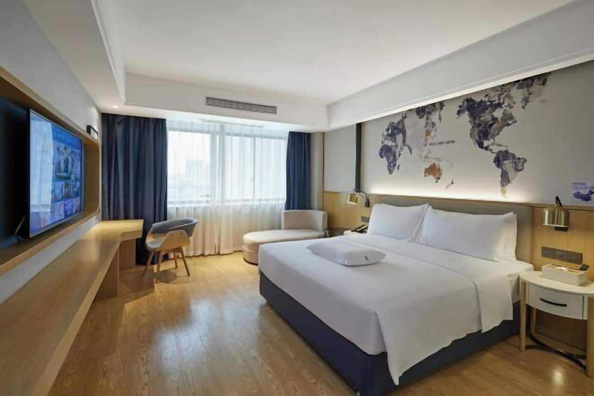 Ein Hotelzimmer mit einem großen Bett, einem Schreibtisch, einem Stuhl, einem Fernseher und einer Weltkarte an der Wand.