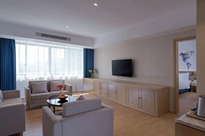 A modern hotel room with a living area featuring a sofa, armchairs, a coffee table, and a flat-screen TV mounted on the wall. - Kyriad Marvelous Hotel (Shenzhen Longhua Guanlan Zhucun Subway Station) (Shenzhen)
