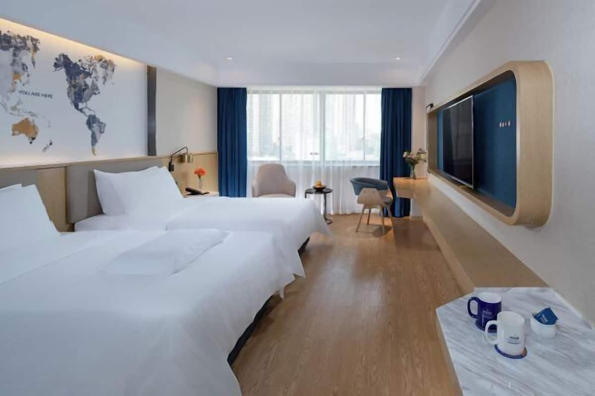 Ein Hotelzimmer mit zwei Betten, einem großen Fernseher, einer Weltkarte an der Wand und Blick auf die Stadt durch das Fenster.