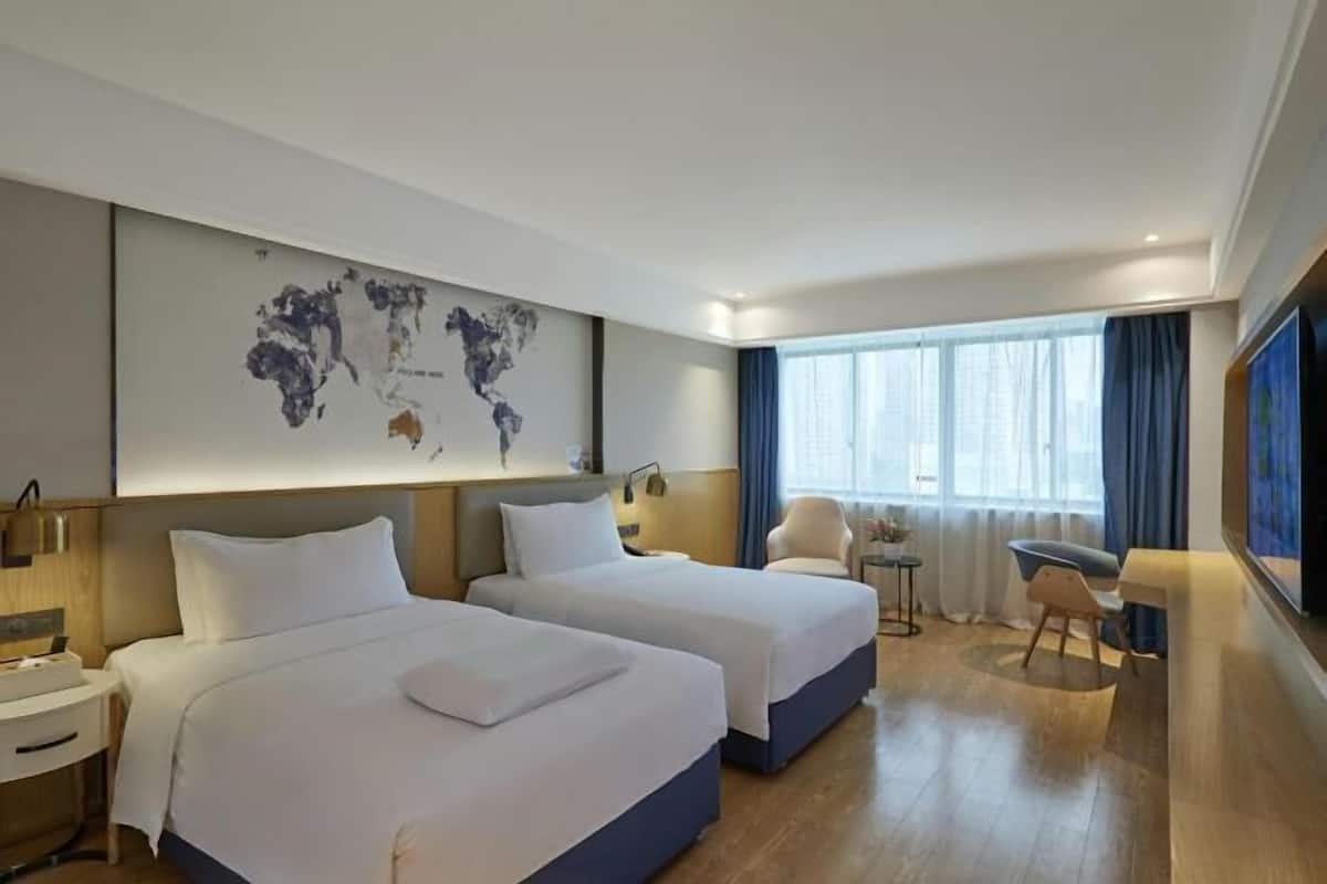 Ein Hotelzimmer mit zwei Betten, einem Schreibtisch, einem Stuhl, einer Weltkarte an der Wand und einem großen Fenster mit Vorhängen.
