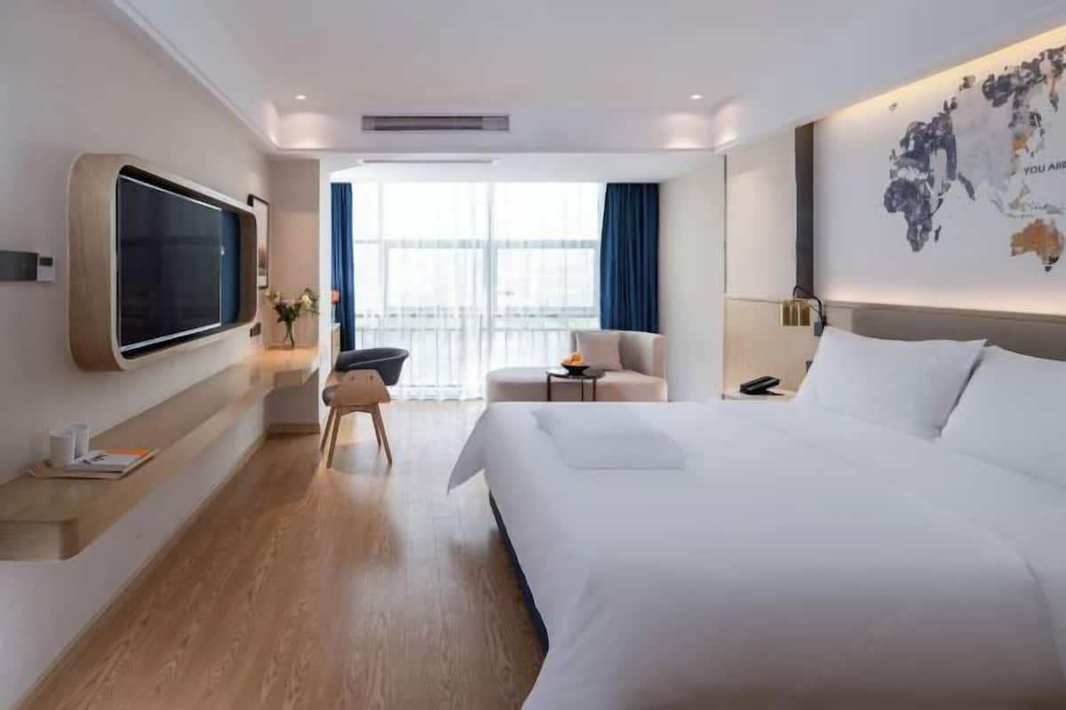 Ein modernes Hotelzimmer mit einem großen Bett, einem flachbildfernseher an der Wand, einer Sitzecke mit Sessel und Tisch sowie einem großen Fenster mit Blick.