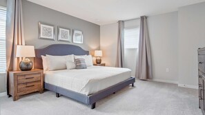 Een slaapkamer met een bed, twee nachtkastjes, een dressoir en drie ingelijste foto's aan de muur.