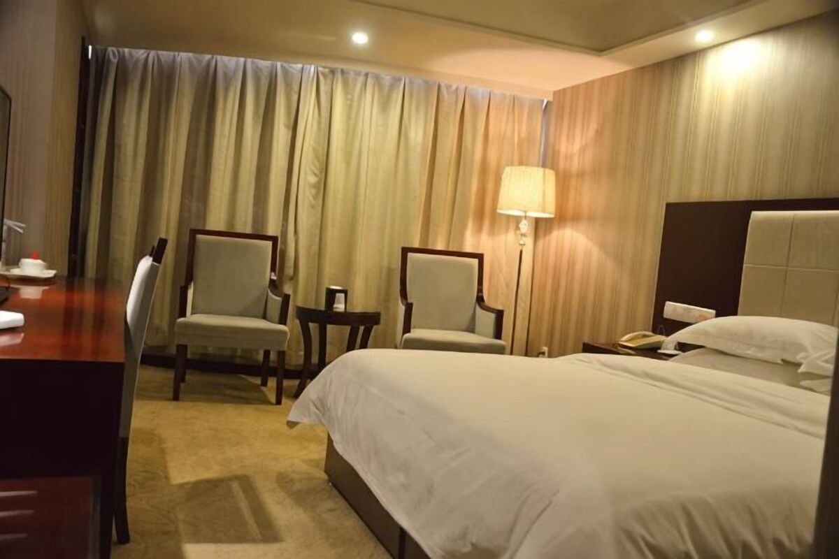 A hotel room with a bed, two armchairs, a small table, a lamp, and a telephone.