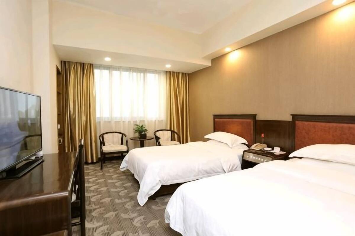 Een hotelkamer met twee bedden, een bureau, een televisietoestel en een raam met gordijnen.