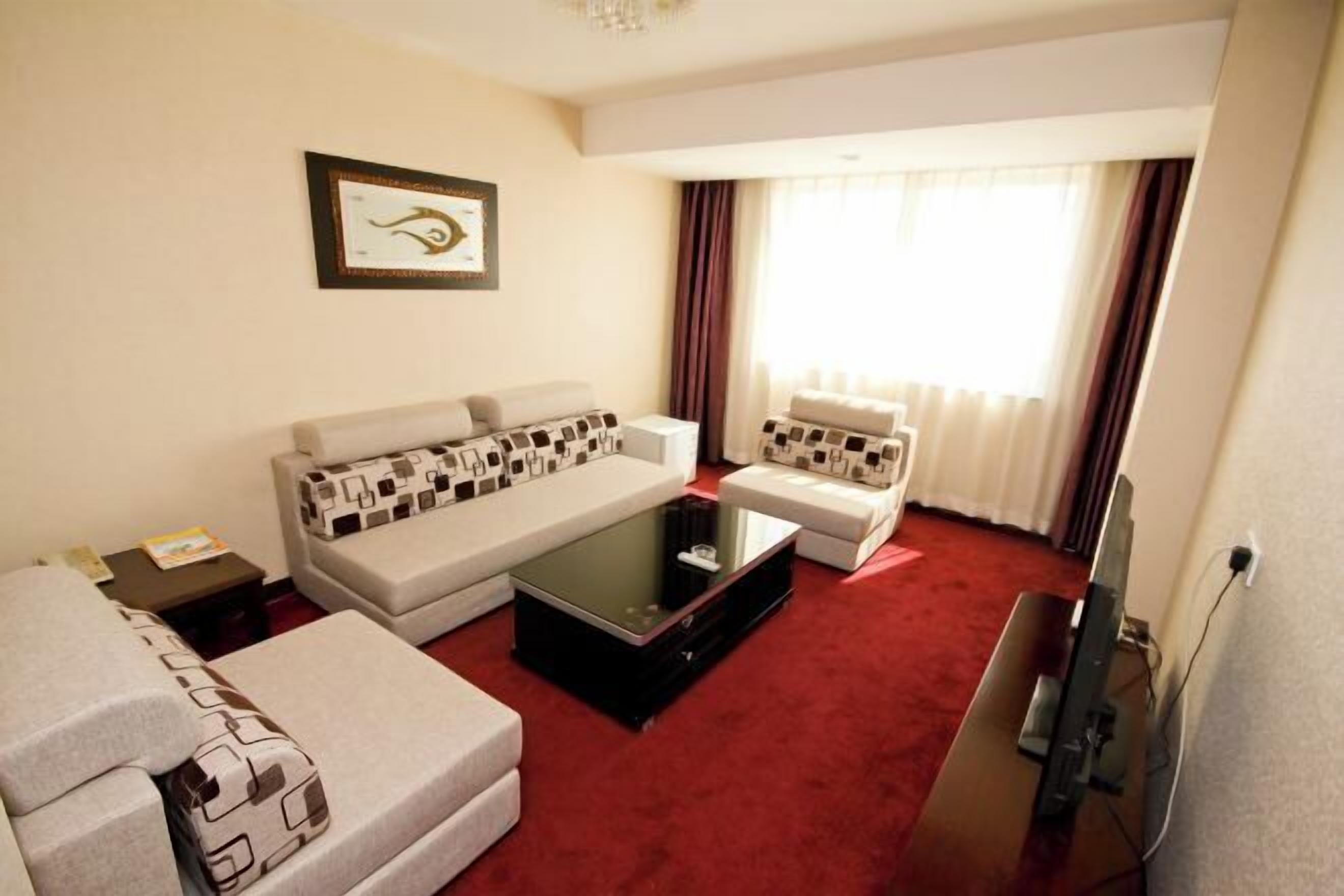A hotel room with a sofa set, a coffee table, a flat-screen TV, and a framed picture on the wall.