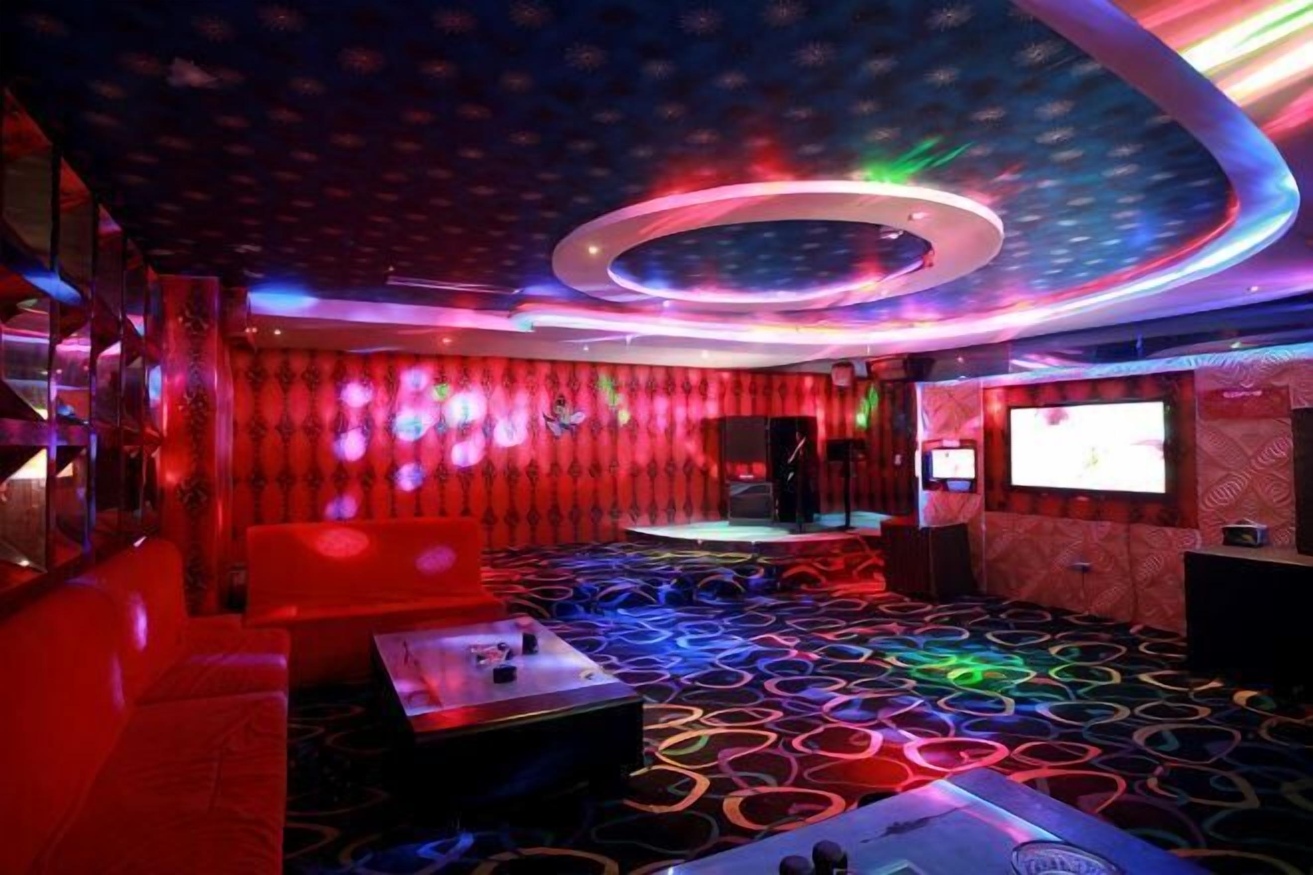A room with a circular ceiling light, a stage, and a large screen.